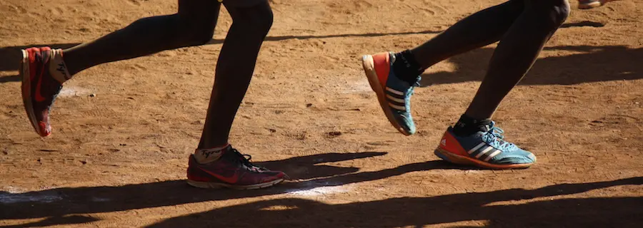 A close up of two feet in sneakers on dirt.