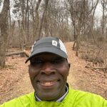 A man in yellow jacket standing on dirt road.